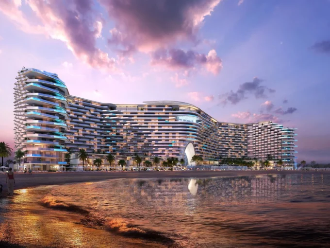 Luxury beachfront towers at sunset with flowing curves, palm trees, and lights at Sora Beach Residences.