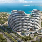 "Aqua Arc," a pair of curved, modern buildings, stands near a coastline with blue water and lush greenery.