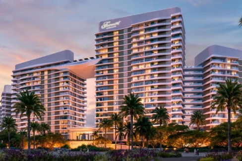 Modern beachfront Fairmont Villas building at sunset, framed by palm trees and lush gardens.