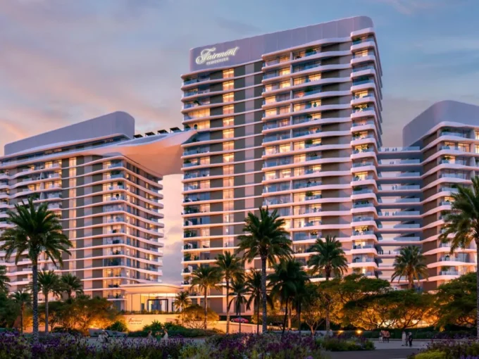 Modern beachfront Fairmont Villas building at sunset, framed by palm trees and lush gardens.