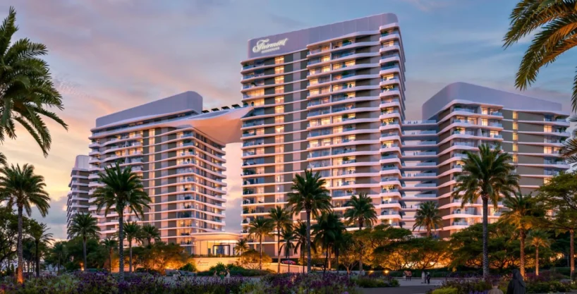 Modern beachfront Fairmont Villas building at sunset, framed by palm trees and lush gardens.