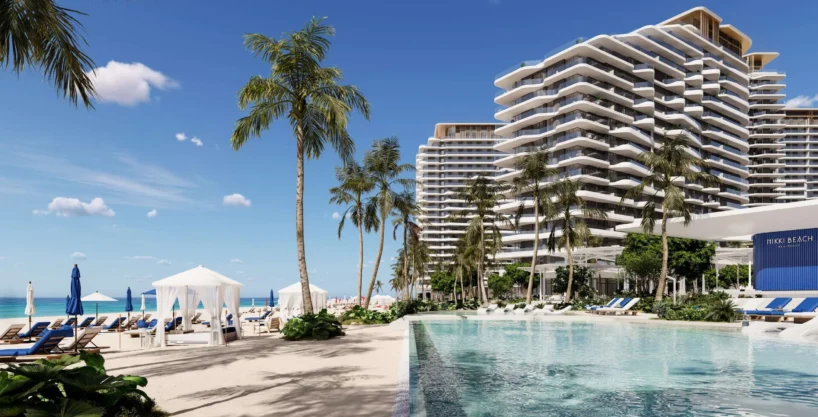 A sunny beach scene at Nikki Beach with palm trees, a swimming pool, and modern buildings.