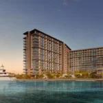Waterfront view of Playa Del Sol luxury residences with yacht and skyline at sunset.