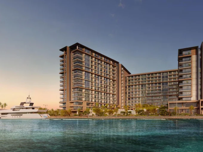 Waterfront view of Playa Del Sol luxury residences with yacht and skyline at sunset.