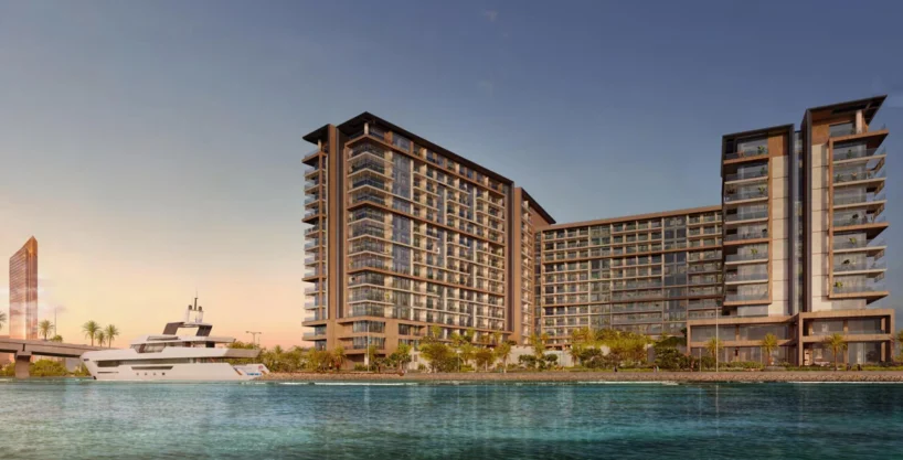 Waterfront view of Playa Del Sol luxury residences with yacht and skyline at sunset.
